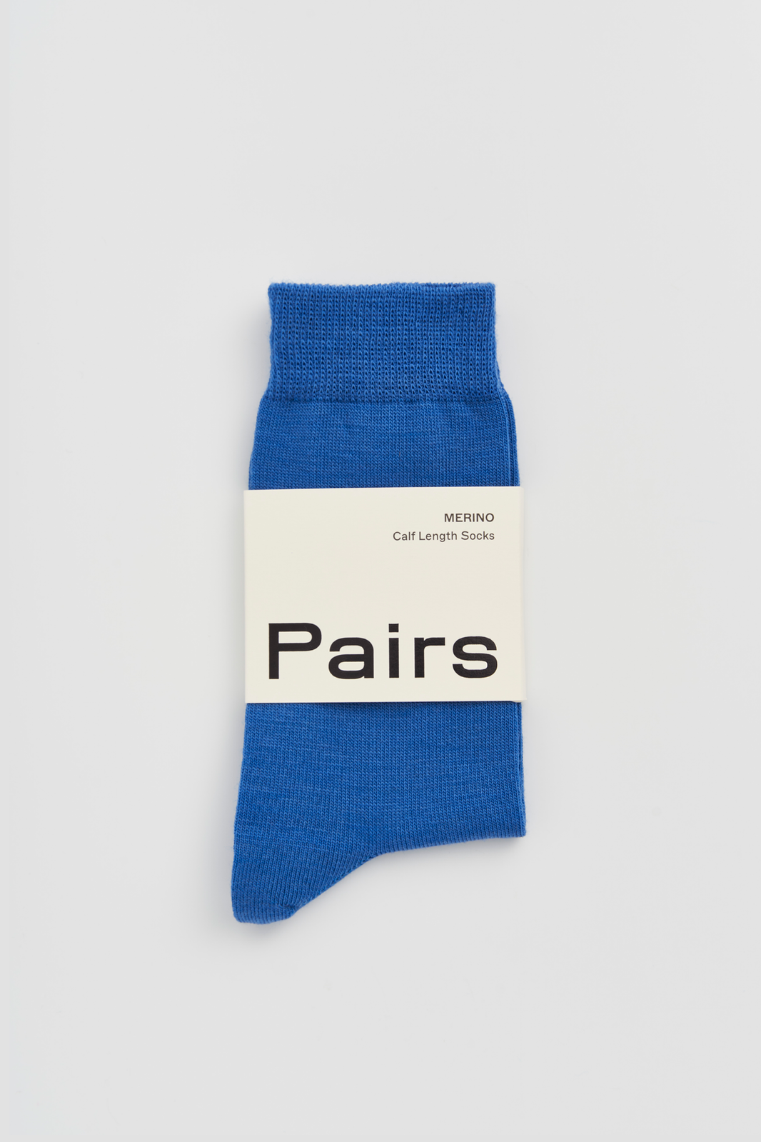 Bright blue calf-length merino sock with a 'Pairs' packaging band on a light grey background