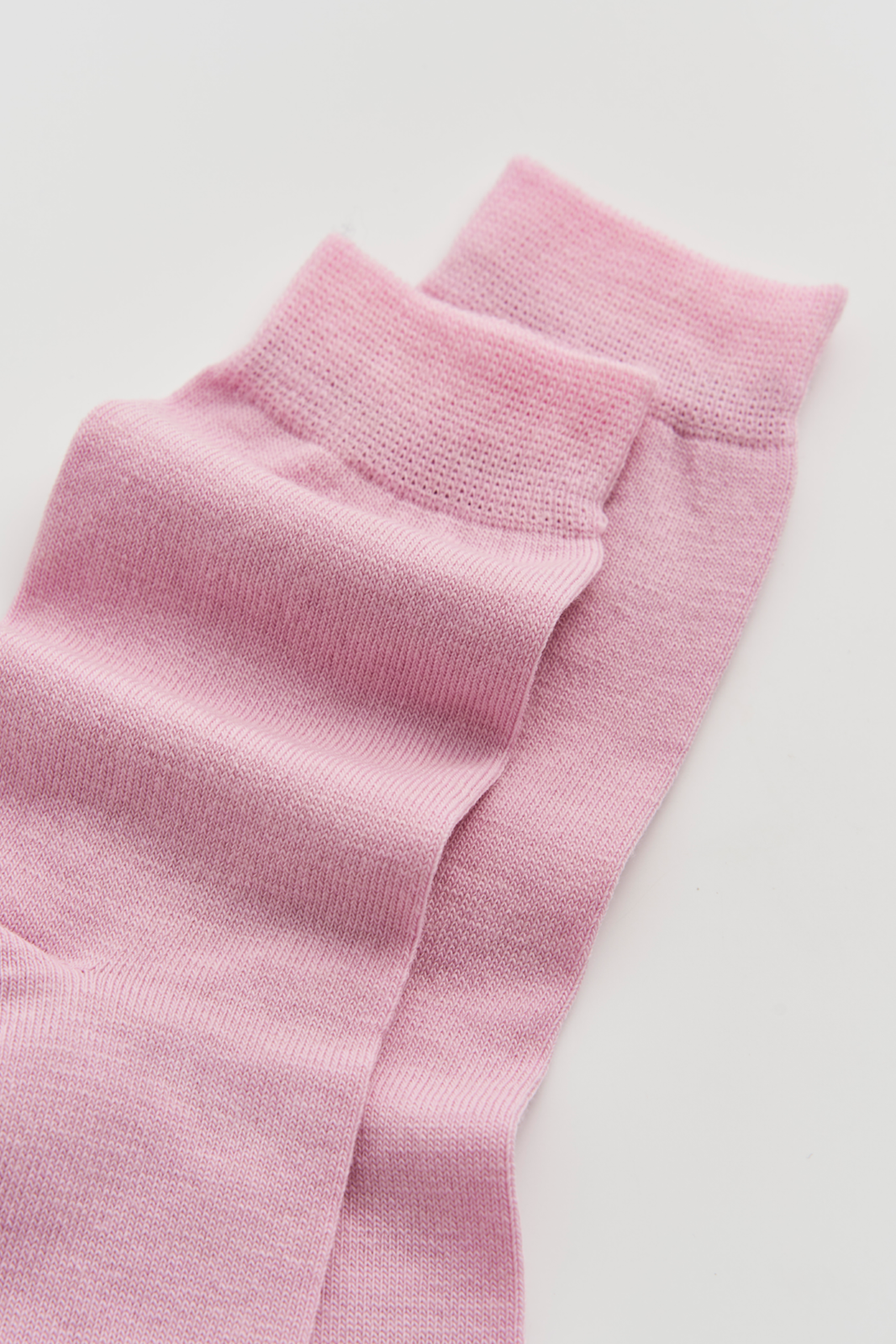 Close-up of a pair of pink calf-length merino socks on a light grey background