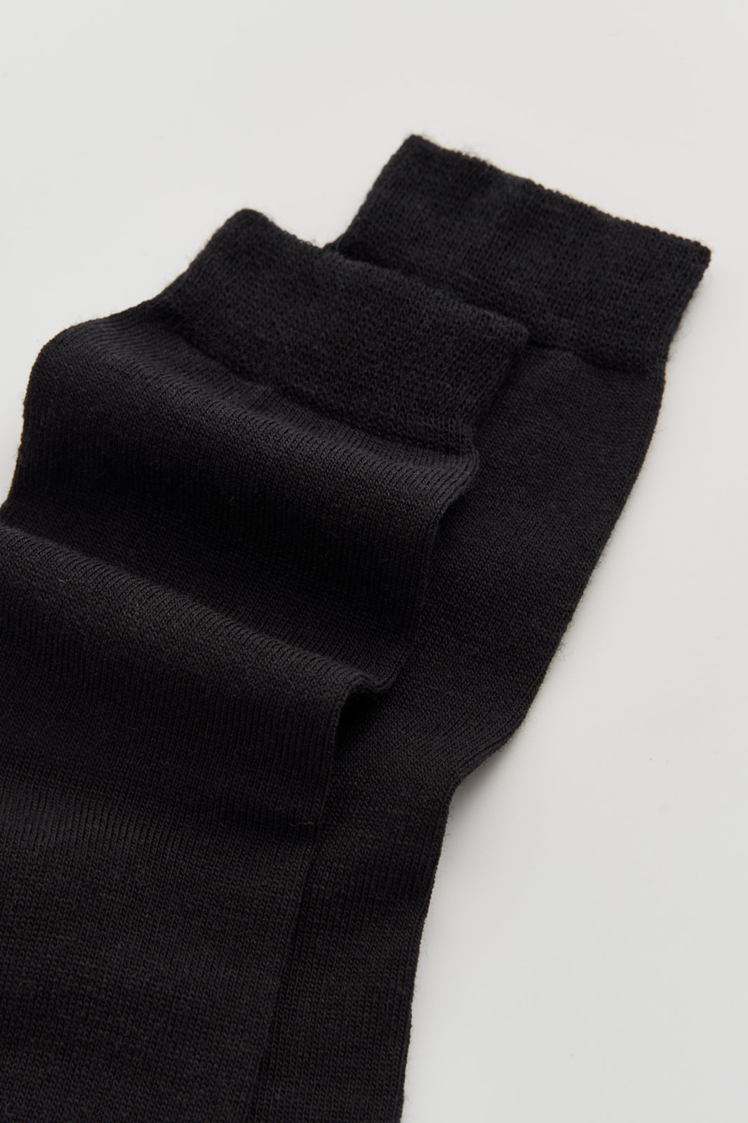 Close-up of the top of a pair of black calf-length merino socks on a light grey background