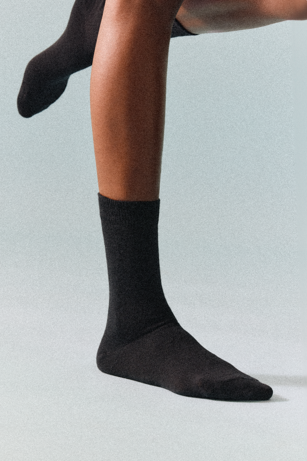 Black calf-length merino socks worn by a person on a light grey background