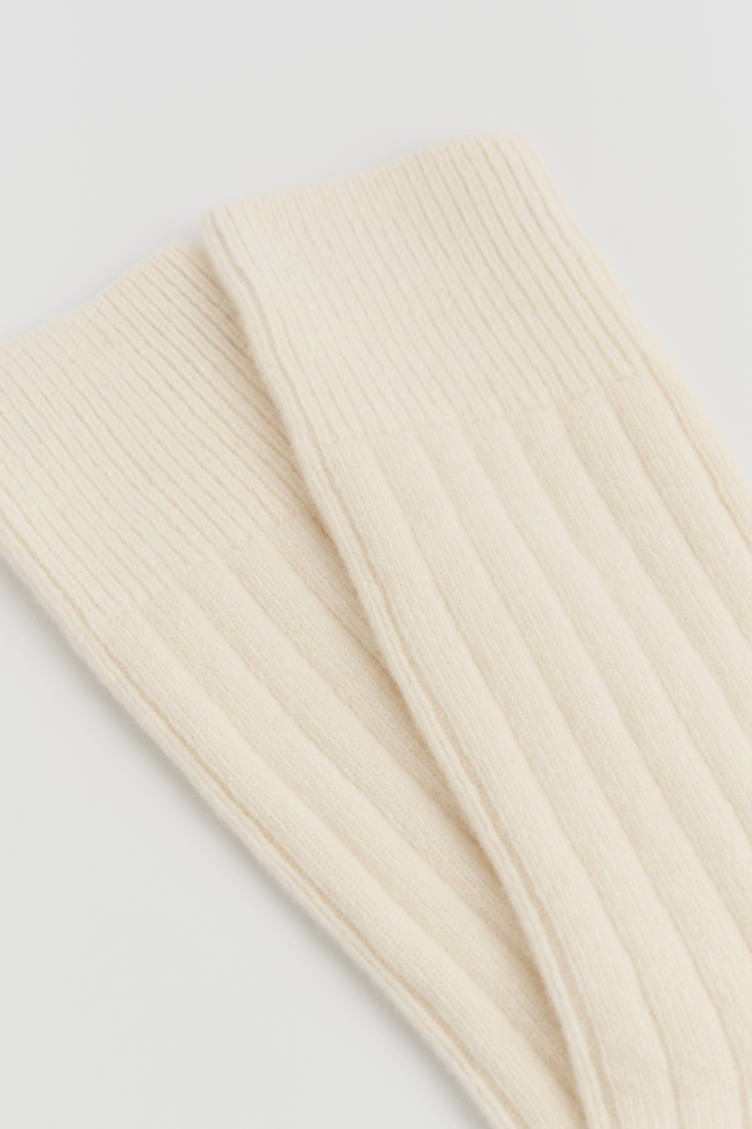 Close-up of a pair of cream merino ribbed bed socks on a light grey background