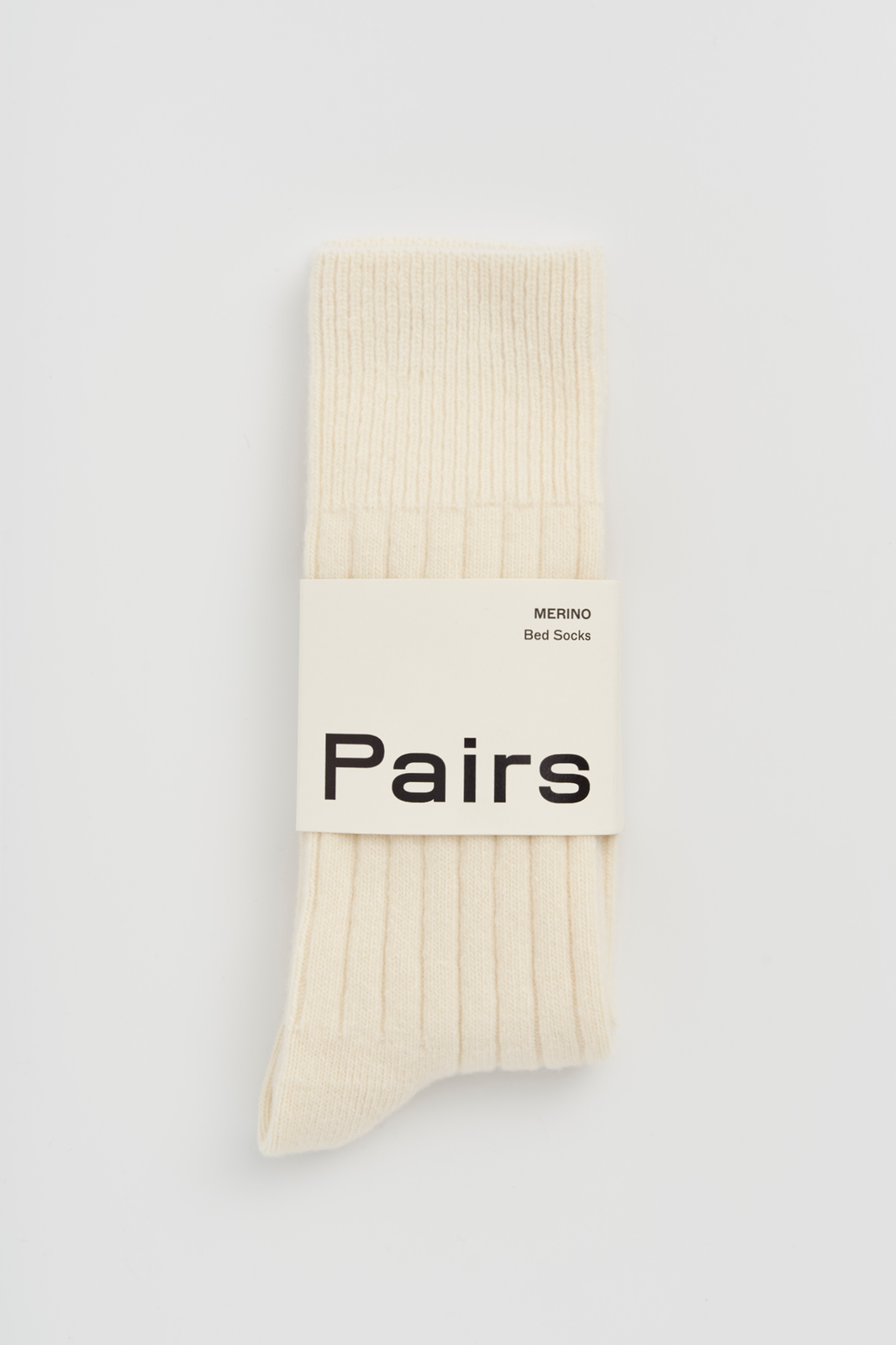 Cream ribbed merino bed sock with a 'Pairs' packaging band on a light grey background
