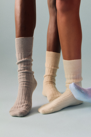 Two pairs of legs wearing grey, blue and cream merino ribbed bed socks on a white background
