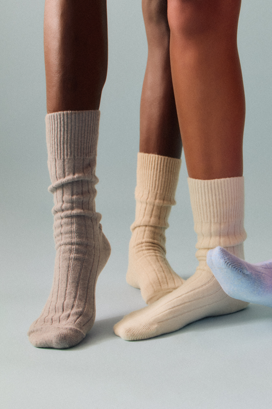 Two pairs of legs wearing grey, blue and cream merino ribbed bed socks on a white background