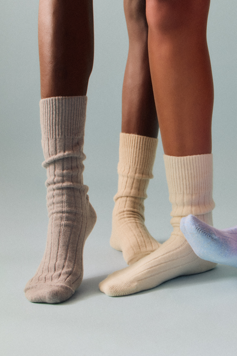 Two pairs of legs wearing grey, blue and cream merino ribbed bed socks on a white background