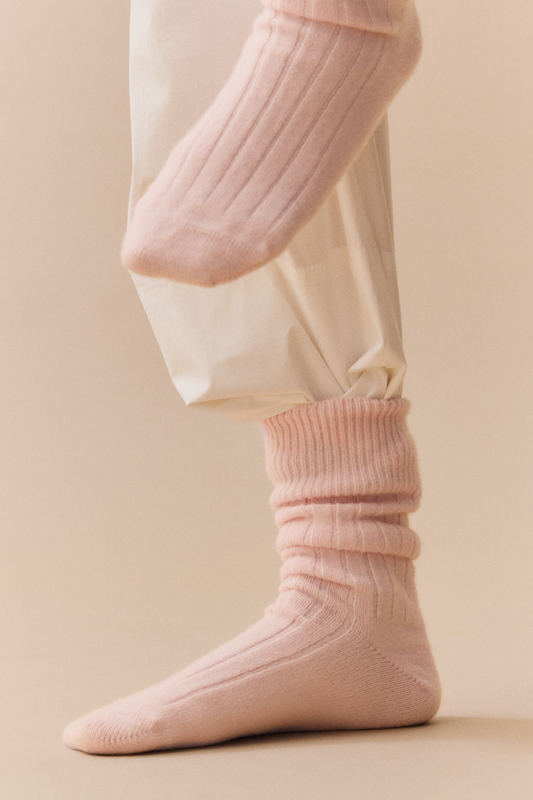 Pale pink ribbed merino bed socks and beige trousers on a neutral background