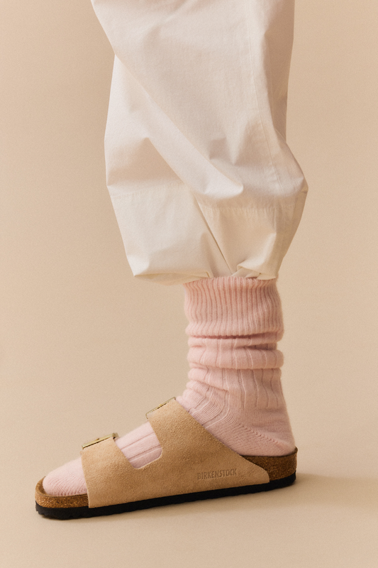 Person wearing beige sandals and pink merino ribbed bed socks on a beige background