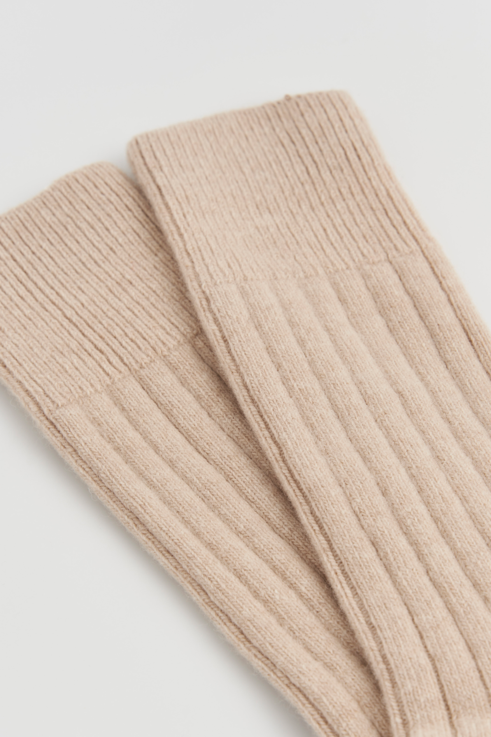Close-up of the top of a pair of light beige merino ribbed bed socks on a light grey background
