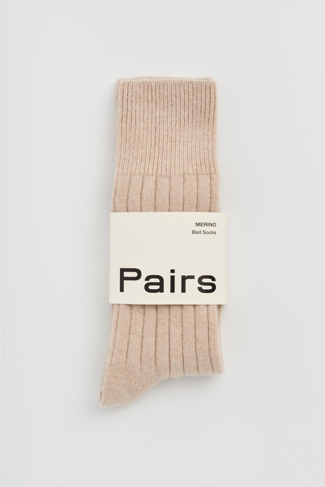Light beige ribbed merino bed sock with a 'Pairs' packaging band on a light grey background