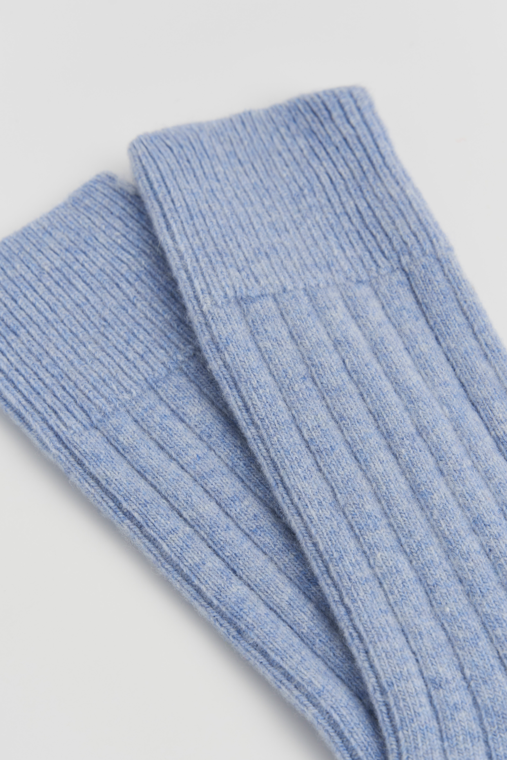 Pair of light blue merino ribbed bed socks on a light grey background