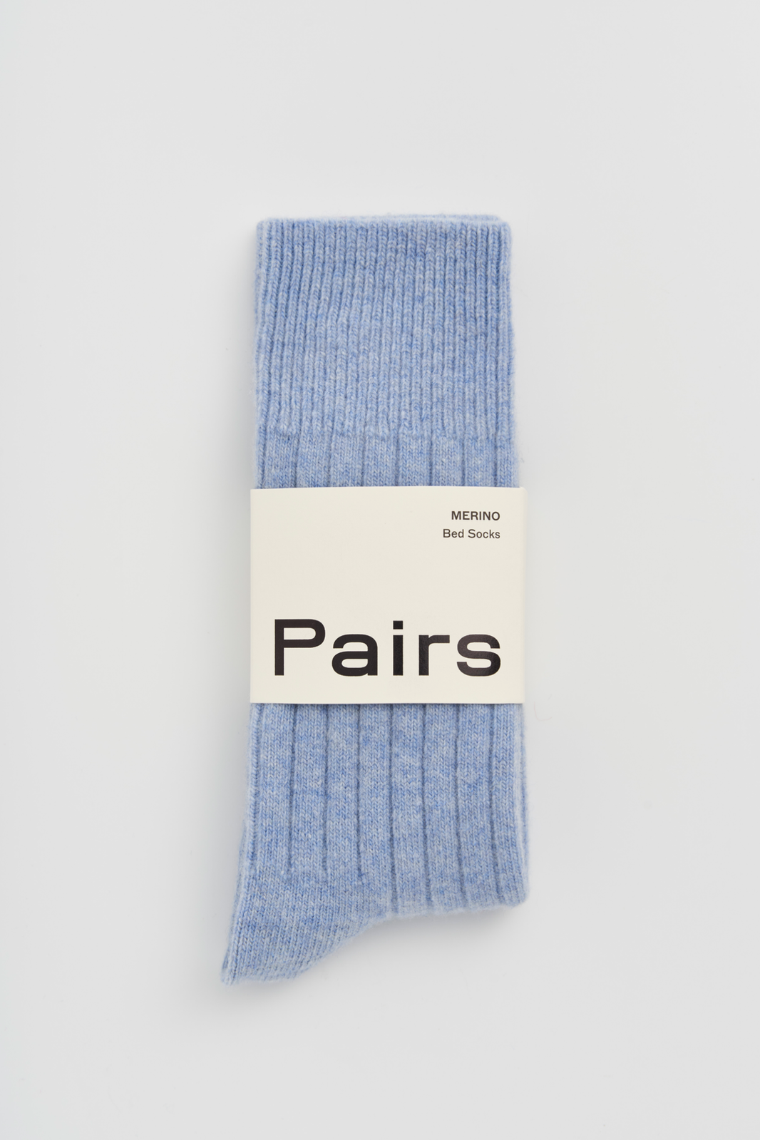 Blue ribbed merino bed sock with a 'Pairs' packaging band on a light grey background