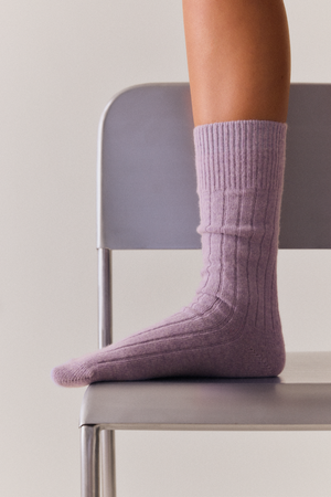 Person wearing a lilac merino ribbed bed sock on a chair with a neutral background