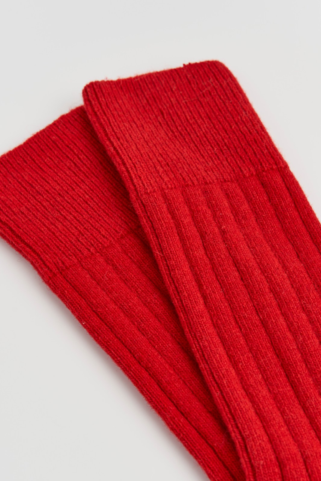 Close-up of the top of a pair of red ribbed merino ribbed bed socks on a light grey background