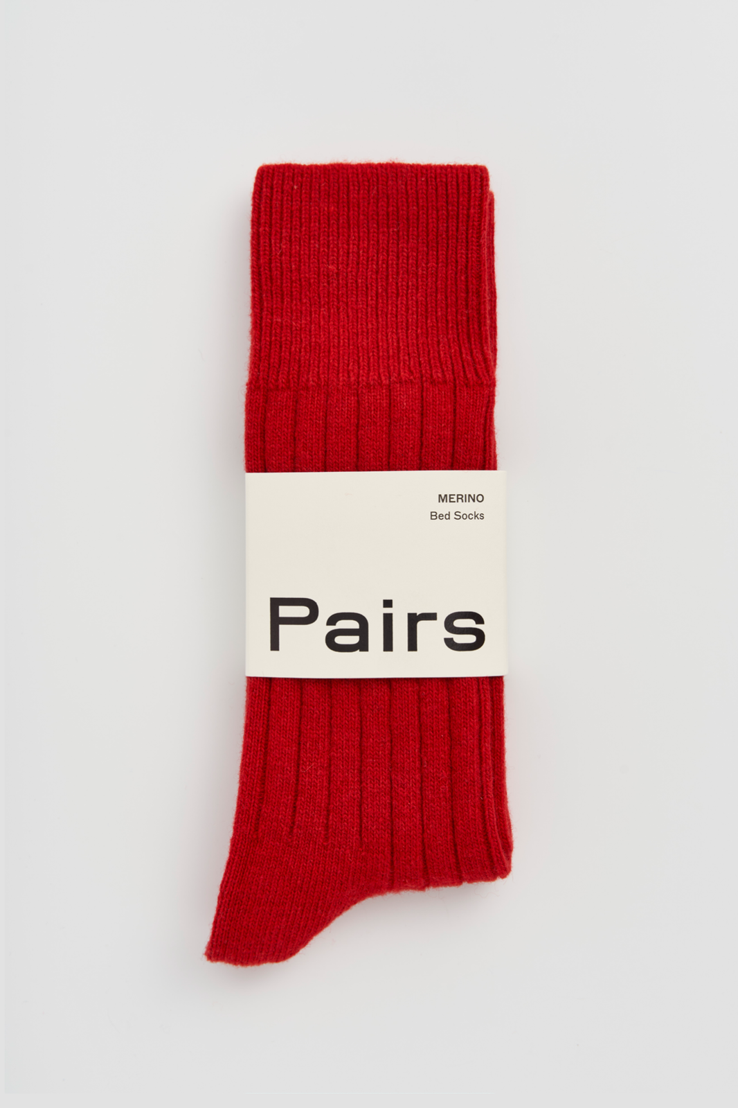 Red ribbed merino bed sock with a 'Pairs' packaging band on a light grey background