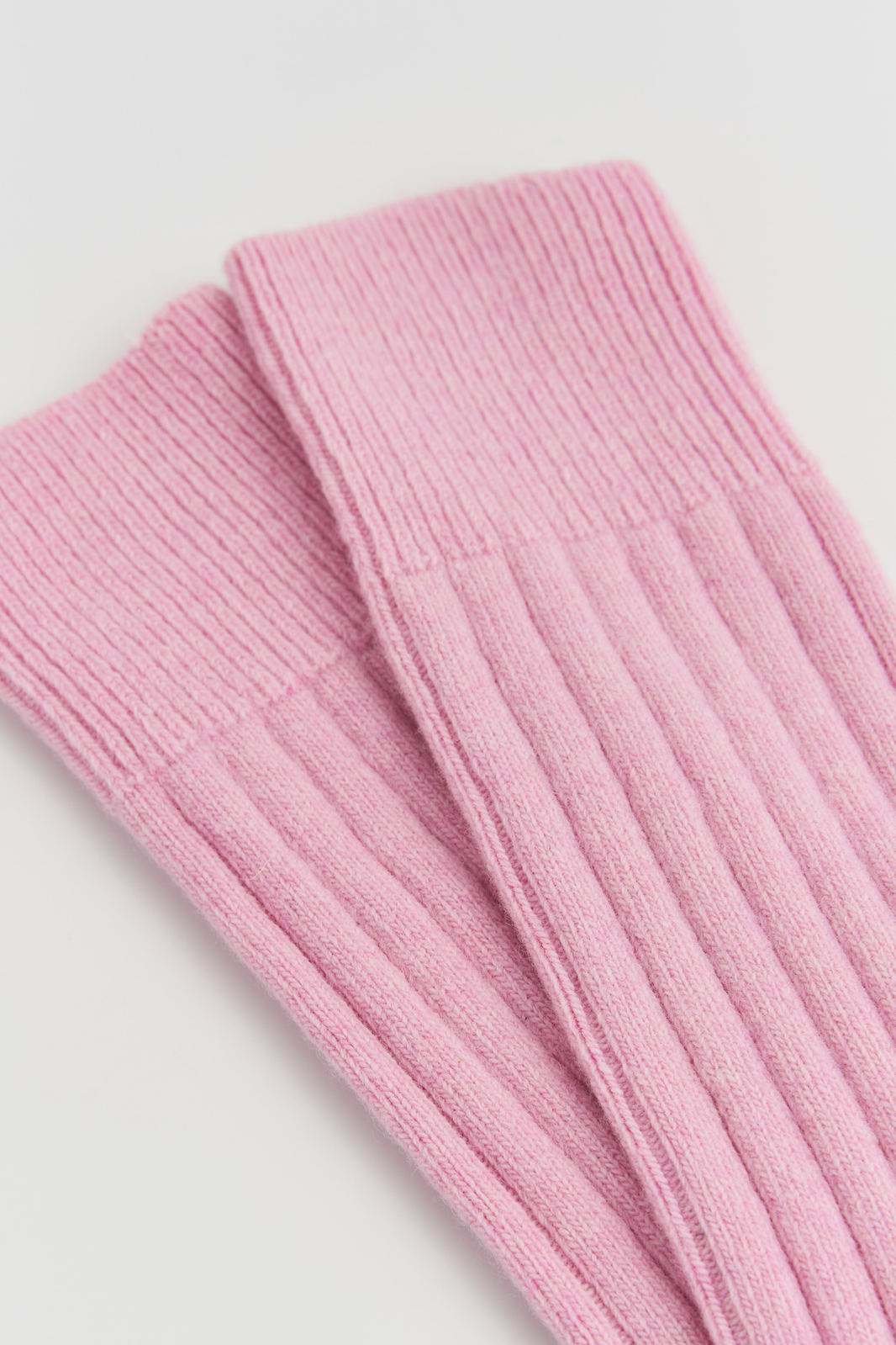 Close-up of the top of a pair of pink merino ribbed bed socks on a light grey background