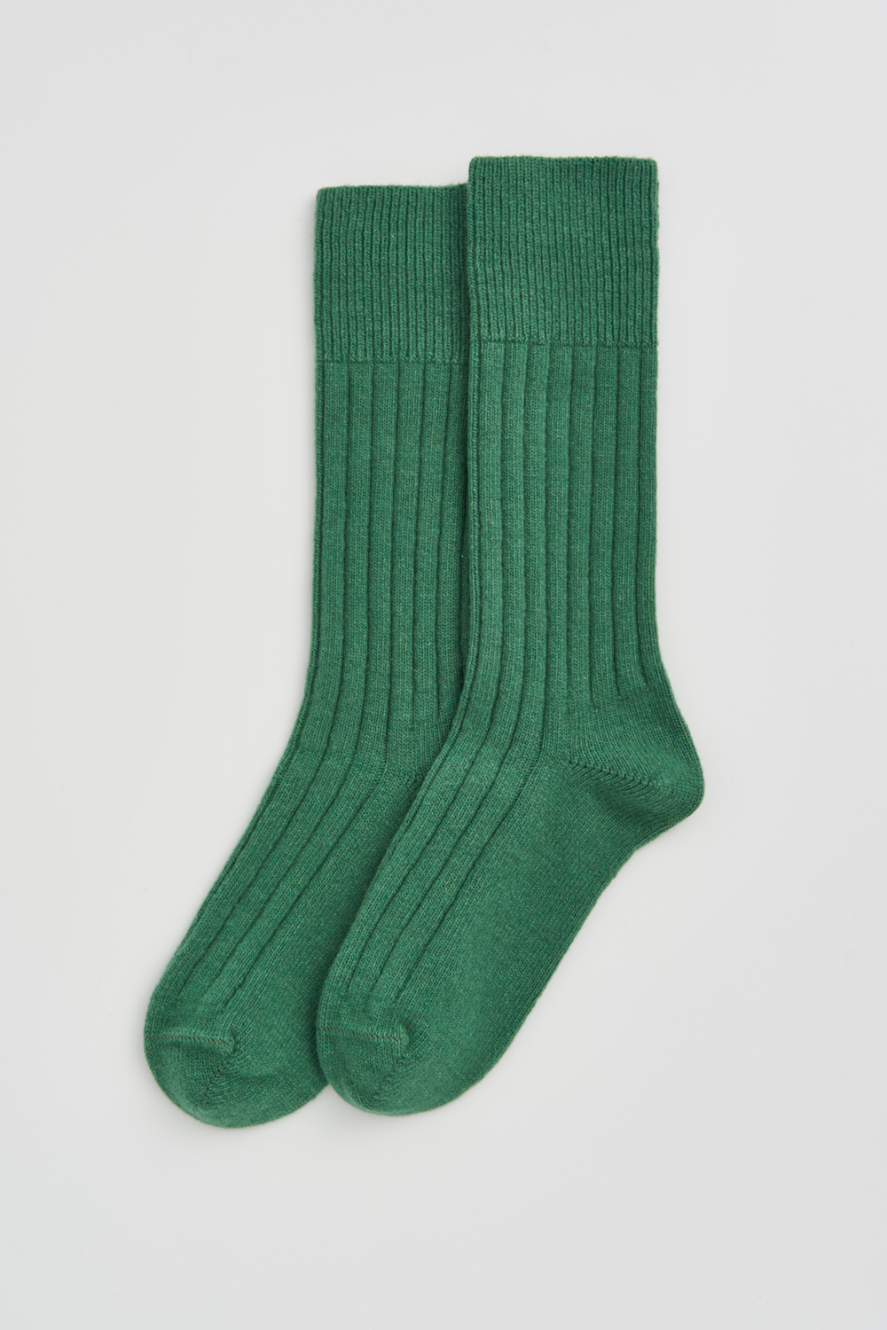 A pair of green merino ribbed bed socks on a light grey background