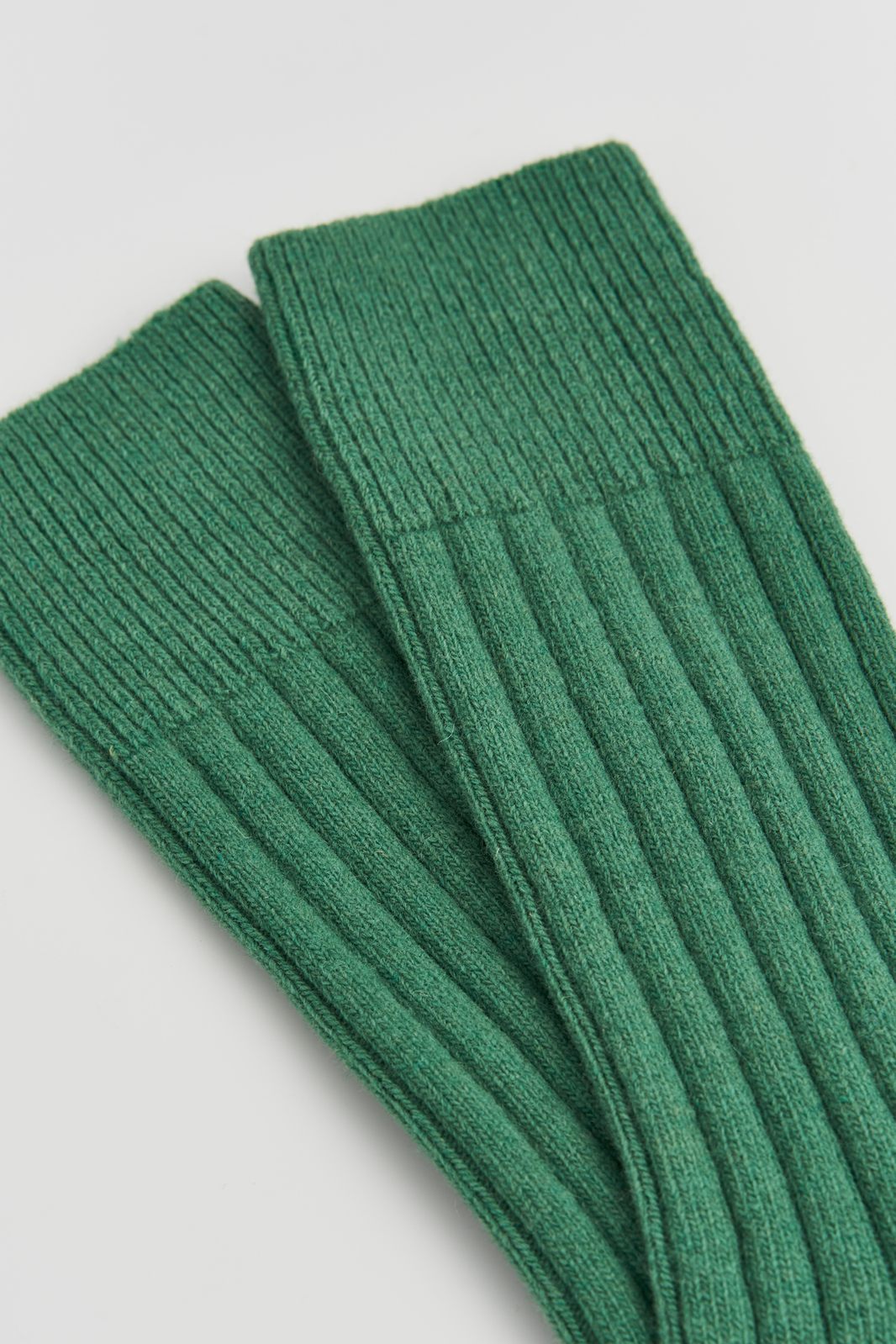 Close-up of the top of a pair of green merino ribbed bed socks on a light grey background