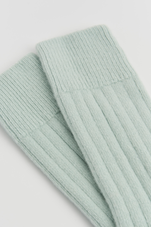 Close-up of the top of a pair of mint green merino ribbed bed socks on a light grey background