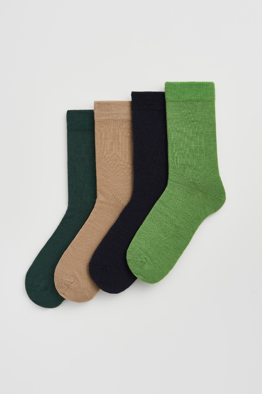 Four pairs of calf-length merino socks in dark green, beige, navy blue, and grass green on a light grey background