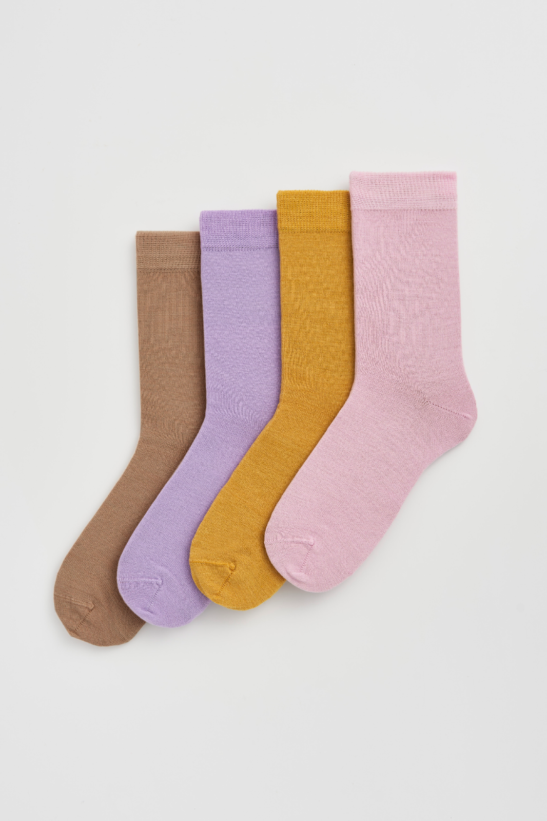 Four pairs of colorful calf-length merino socks in beige, lilac, mustard yellow, and pink on a light grey background.