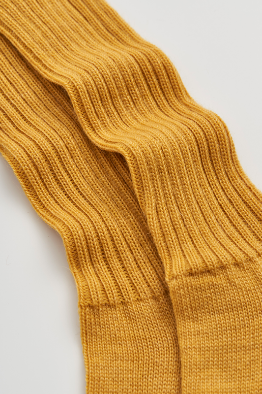 Close-up of a pair of mustard yellow ribbed mohair socks on a light grey background