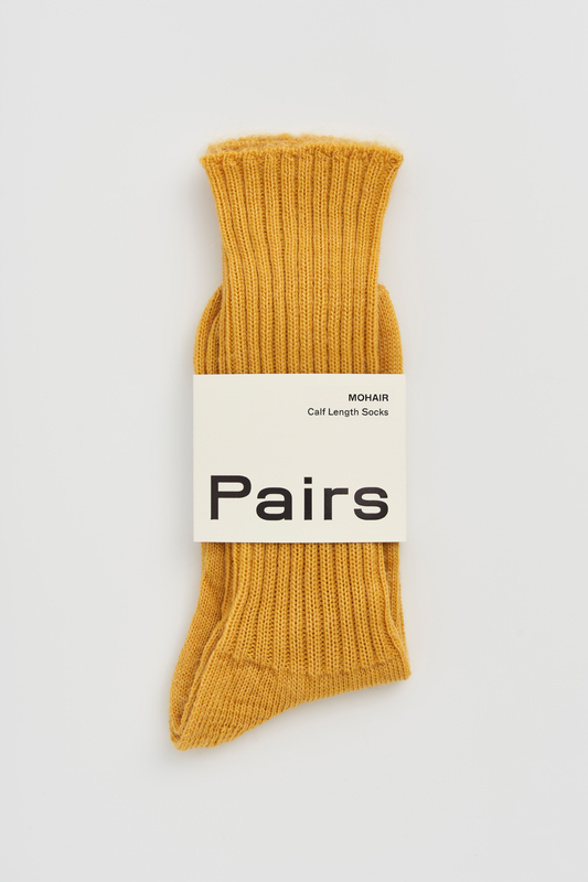 Mustard yellow ribbed mohair socks with a 'Pairs' packaging band on a light grey background