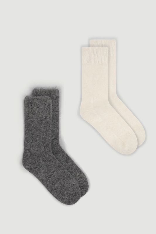Two pairs of ultra soft plain alpaca bed socks, one grey and one cream, on a white  background.