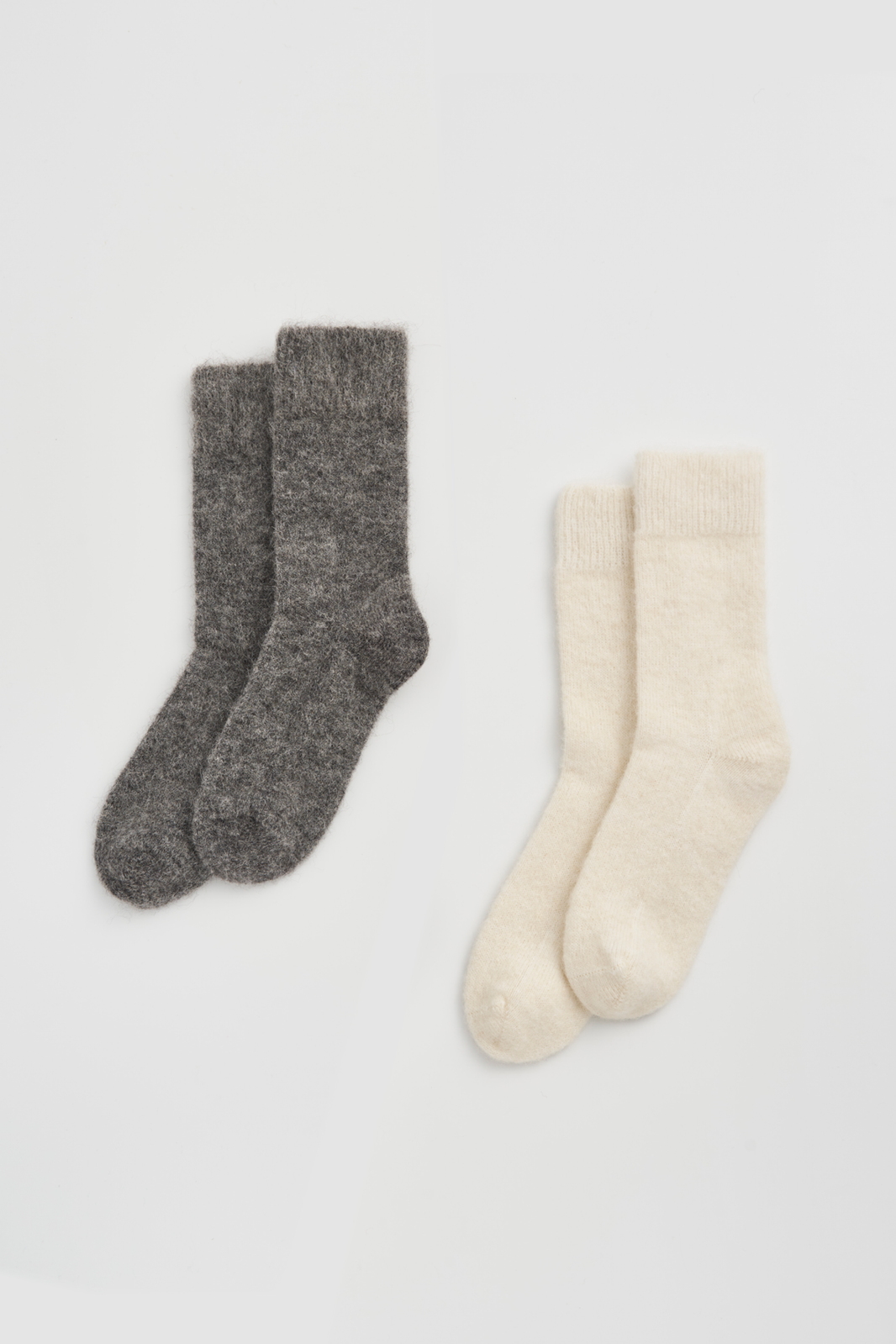Two pairs of plain ultra soft alpaca bed socks, one grey and one cream, on a light grey background.