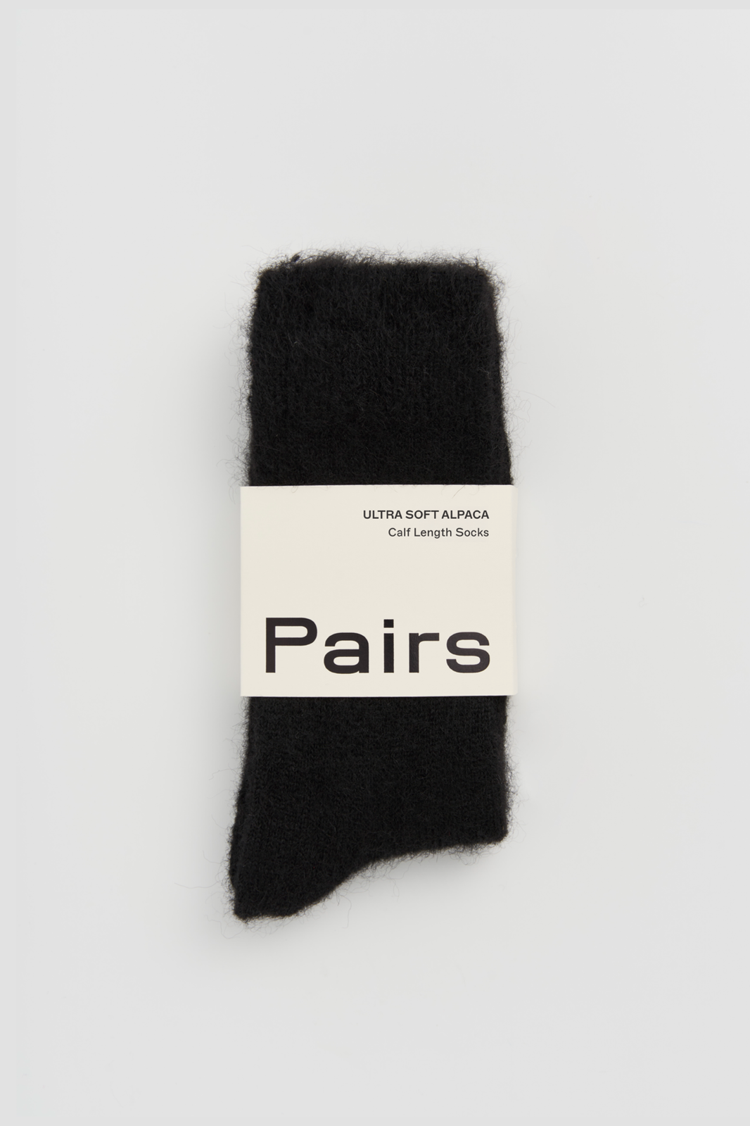 Pair of black ultra soft alpaca socks with a 'Pairs' packaging band on a light grey background