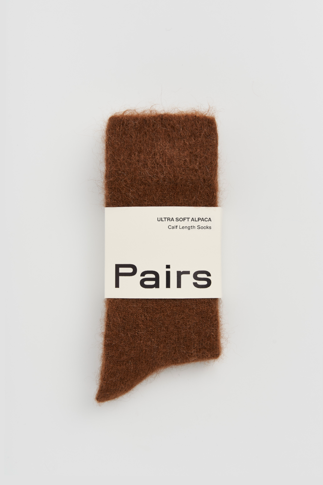 Pair of mid-brown ultra soft alpaca socks with a 'Pairs' packaging band on a light grey background