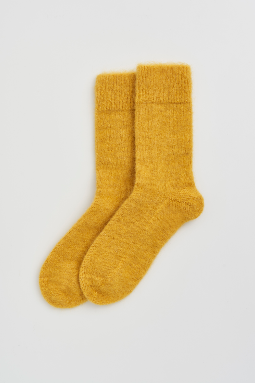 Pair of mustard yellow calf-length ultra soft alpaca socks on a light grey background
