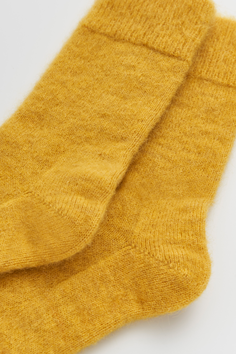 Close-up of a pair of mustard yellow calf-length ultra soft alpaca socks on a light grey background