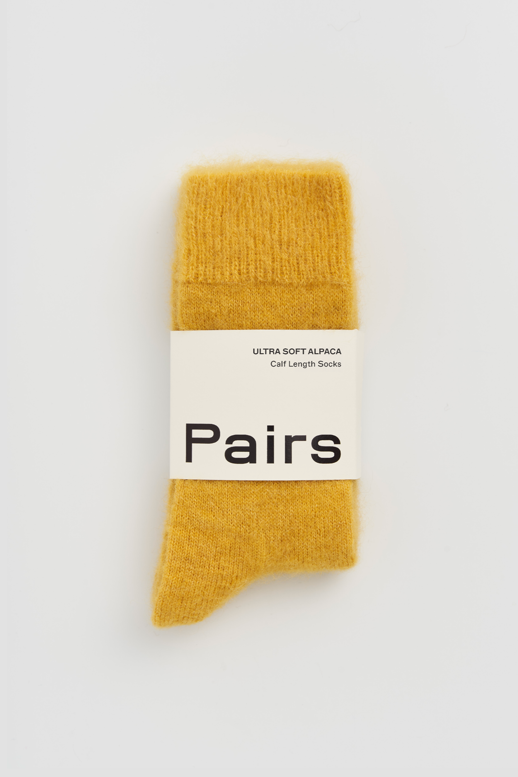 Mustard yellow calf-length ultra soft alpaca sock with 'Pairs' packaging band on a white background
