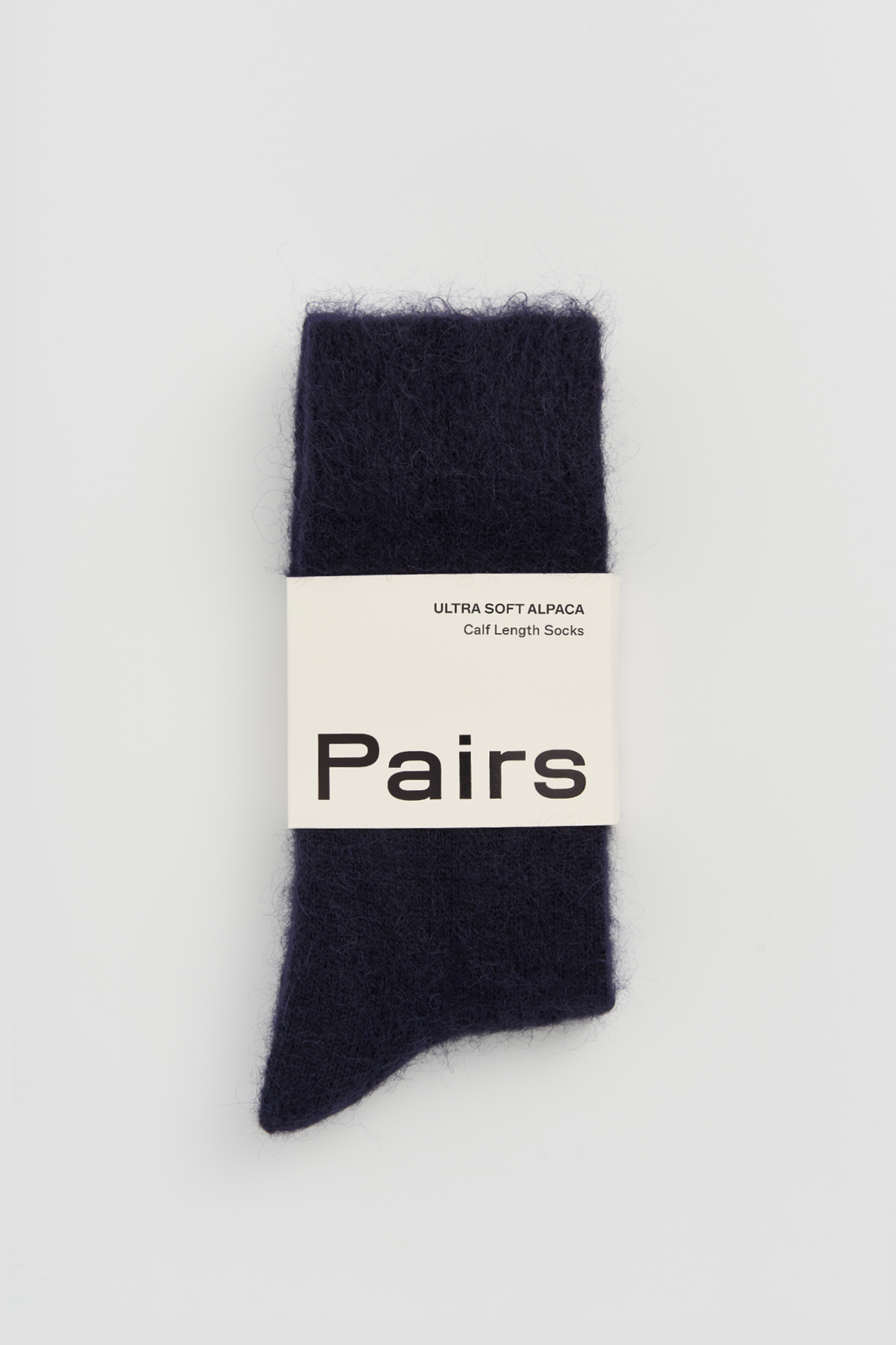 Pair of navy ultra soft alpaca socks with a 'Pairs' packaging band on a light grey background