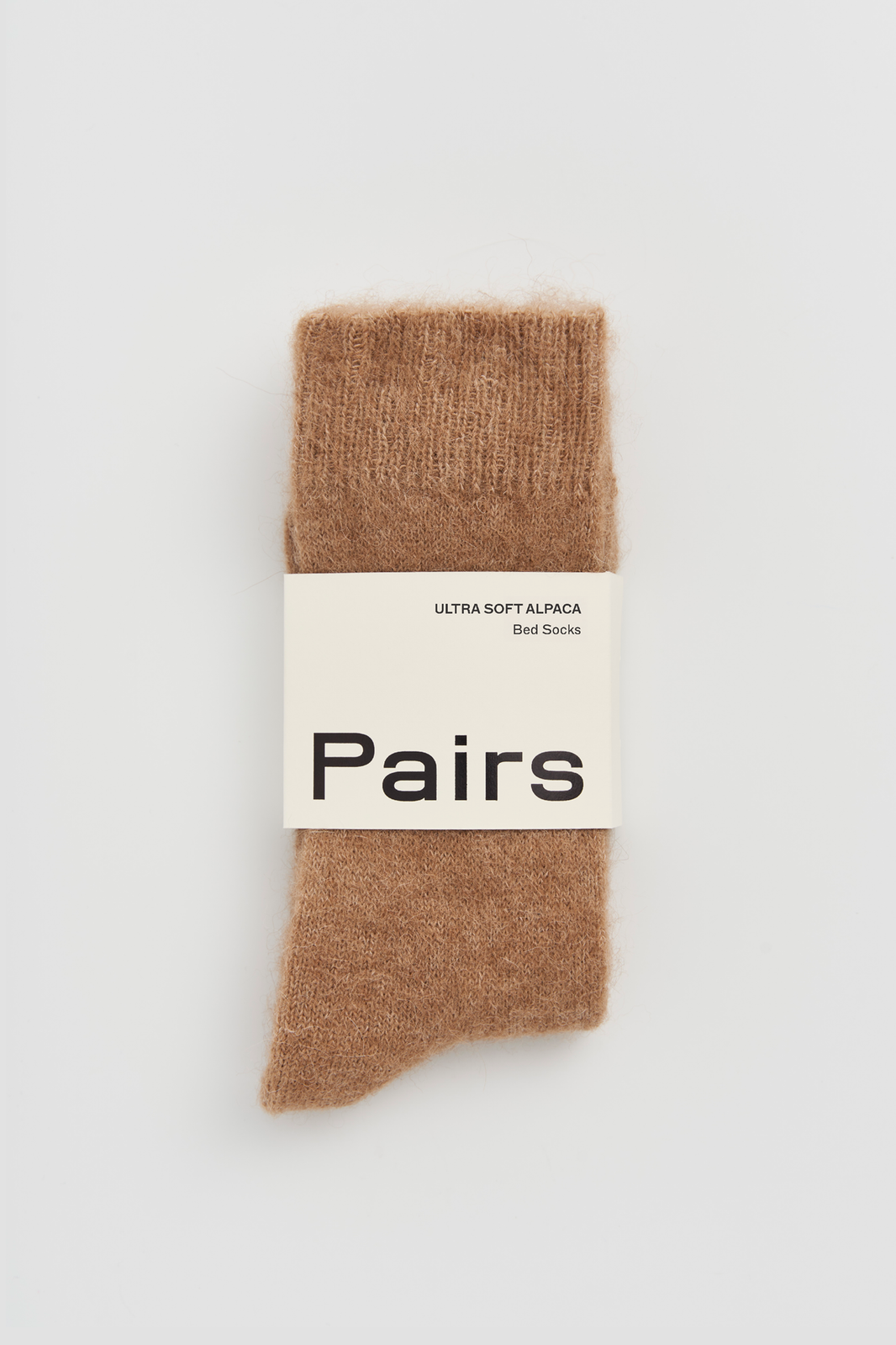 Pair of light brown ultrasoft alpaca bed socks with a 'Pairs' packaging band on a light grey background