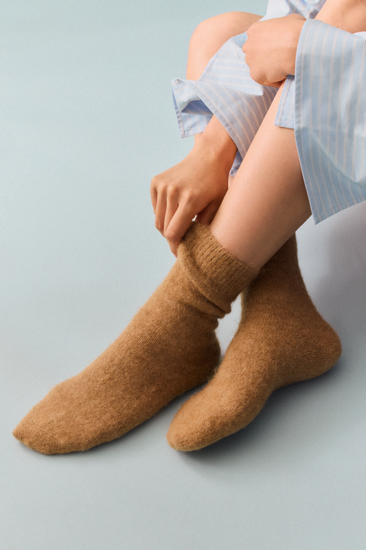 Person wearing light brown ultra soft plain alpaca bed socks on a white background