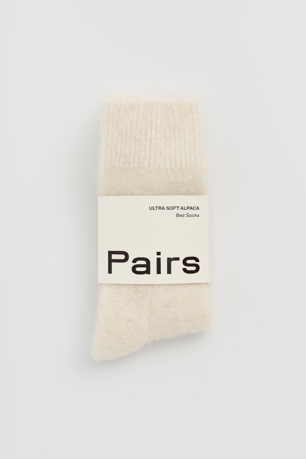 Pair of cream ultra soft alpaca bed socks with a 'Pairs' packaging band on a light grey background
