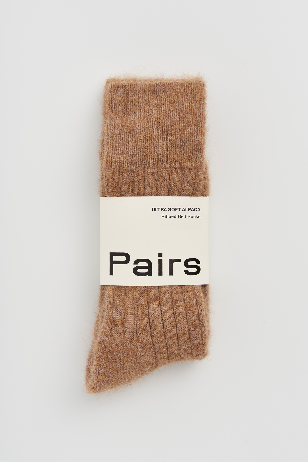 Pair of brown ribbed ultra soft alpaca bed socks with a 'Pairs' packaging band on a light grey background