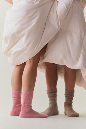 Two people wearing pink and light brown ultra soft ribbed alpaca bed socks with a white background