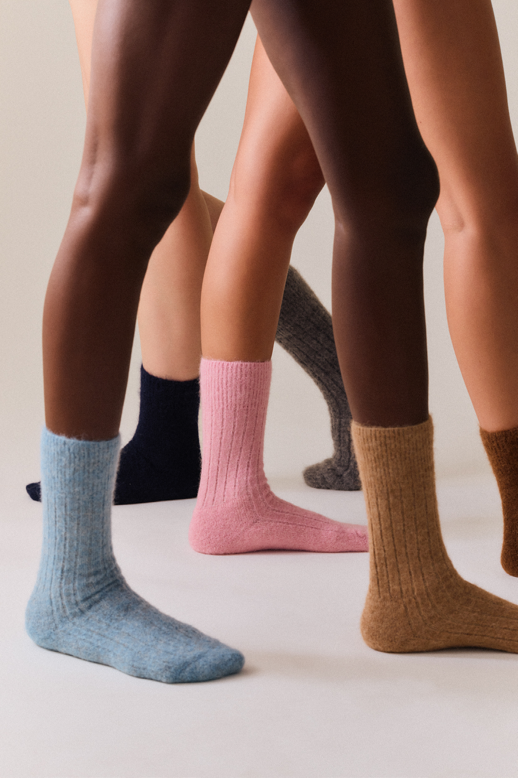 Three people wearing six different socks on a neutral background