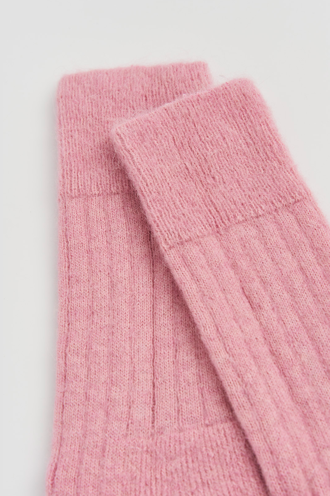 Close-up of the top of a pair of pink ribbed ultra soft alpaca bed socks on a light grey background