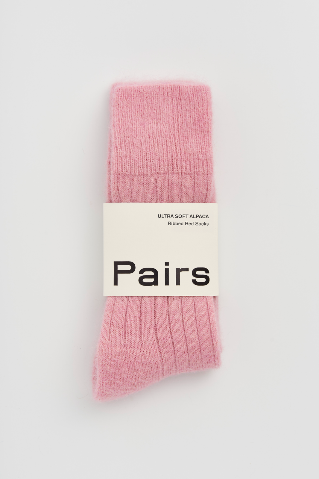Pair of pink ribbed ultra soft alpaca bed socks with a 'Pairs' packaging band on a light grey background