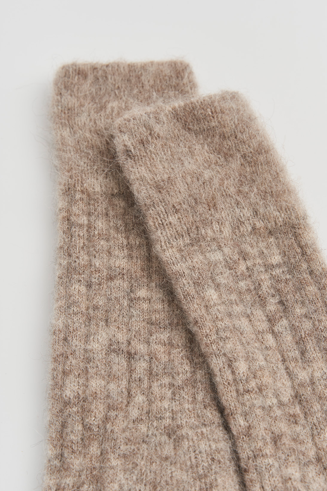 Close-up of the top of a pair of oatmeal ultra soft alpaca ribbed bed socks on a light grey background