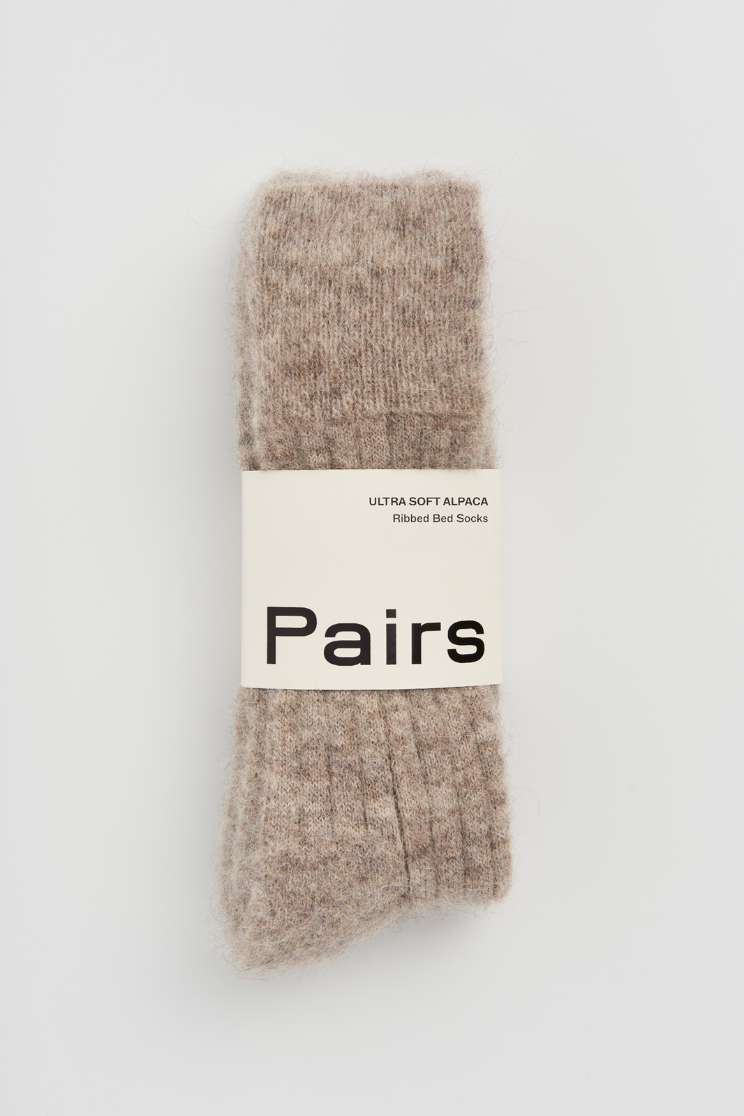 Pair of oatmeal ultra soft alpaca ribbed bed sock with a 'Pairs' packaging band on a light grey background