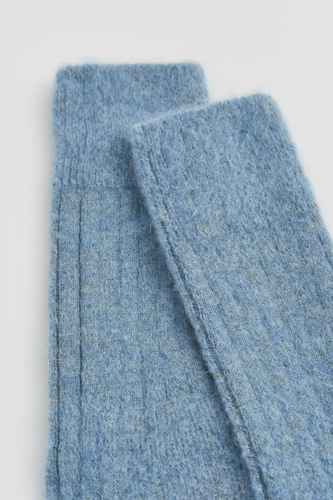 Close-up of the top of a pair of blue ribbed ultra soft alpaca bed socks on a light grey background
