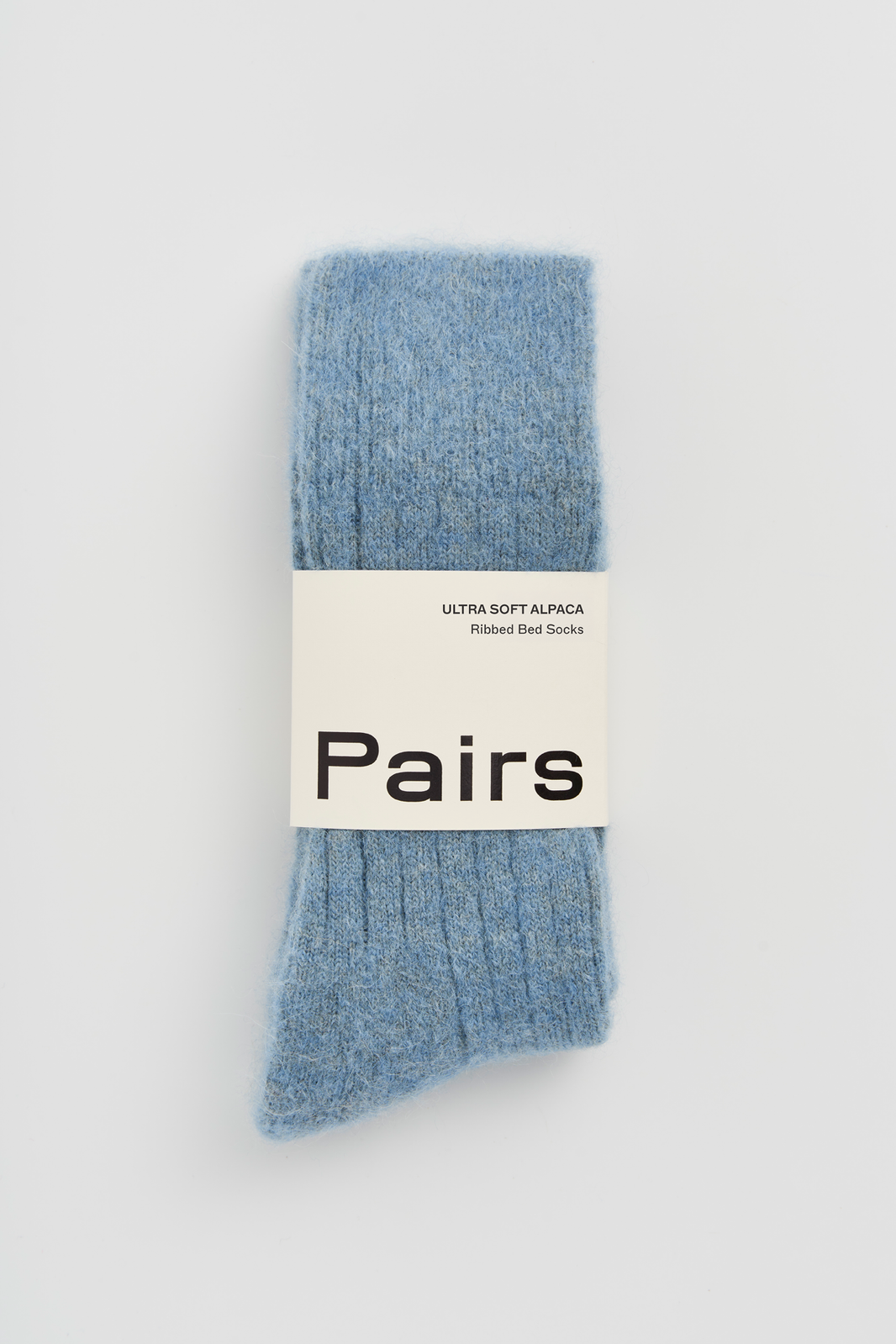 Pair of blue ribbed ultra soft alpaca bed socks with a 'Pairs' packaging band on a light grey background