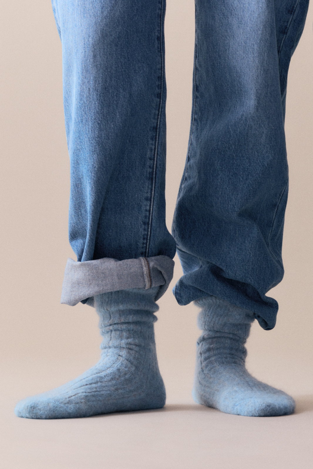 Person wearing blue jeans and blue ribbed ultra soft alpaca bed socks on a beige background