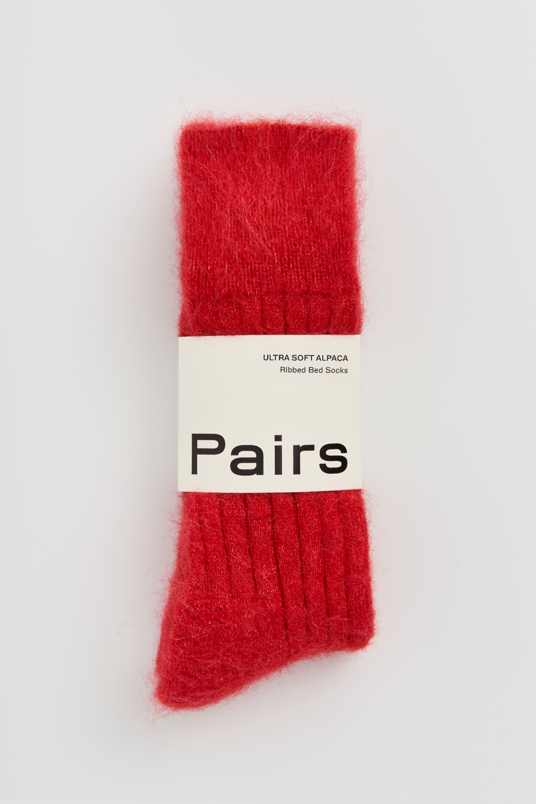 Red ultra soft ribbed alpaca bed sock with a 'Pairs' packaging band on a light grey background