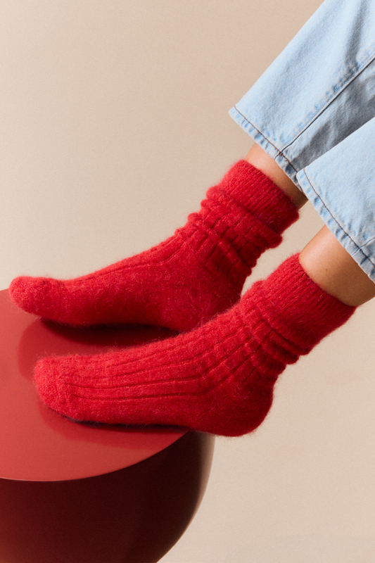 Red ultra soft alpaca ribbed bed socks worn with light blue jeans on a beige background