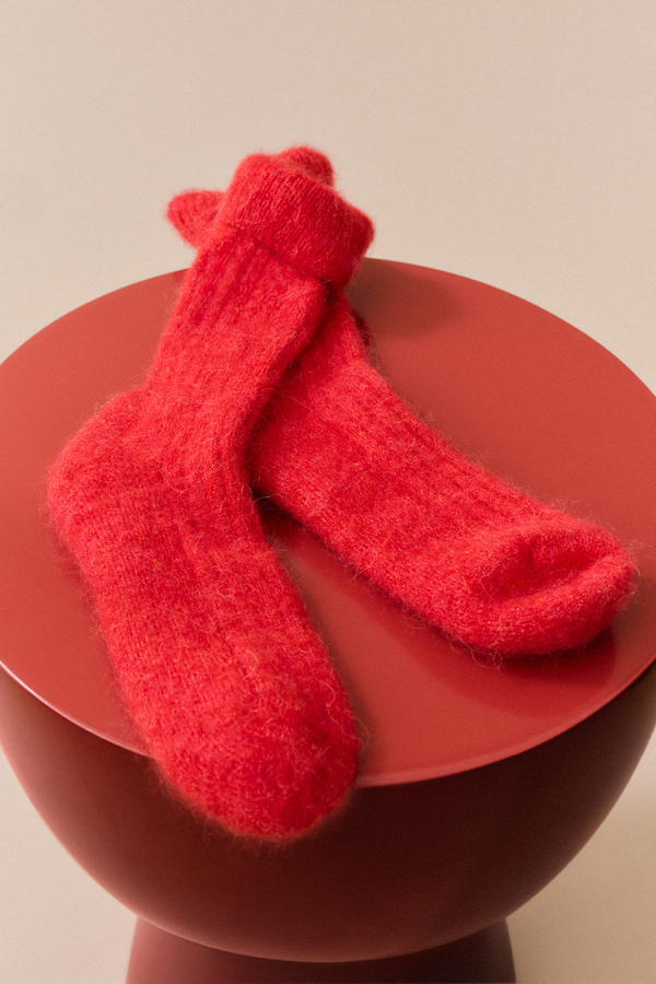 Red ultra soft ribbed alpaca bed socks on a red stool against a beige background
